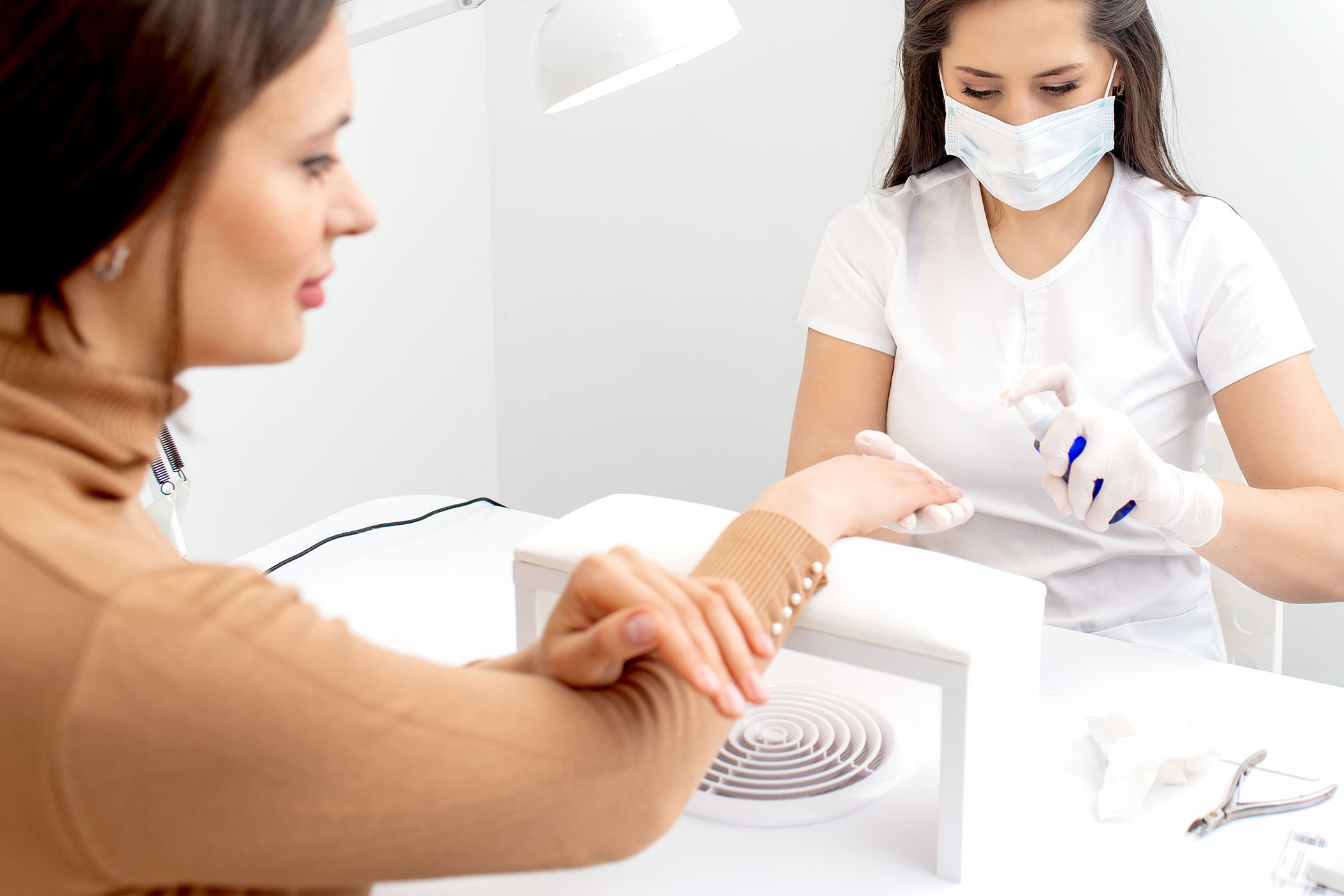 nail technician wearing proetctive face mask doing manicure in beauty salon