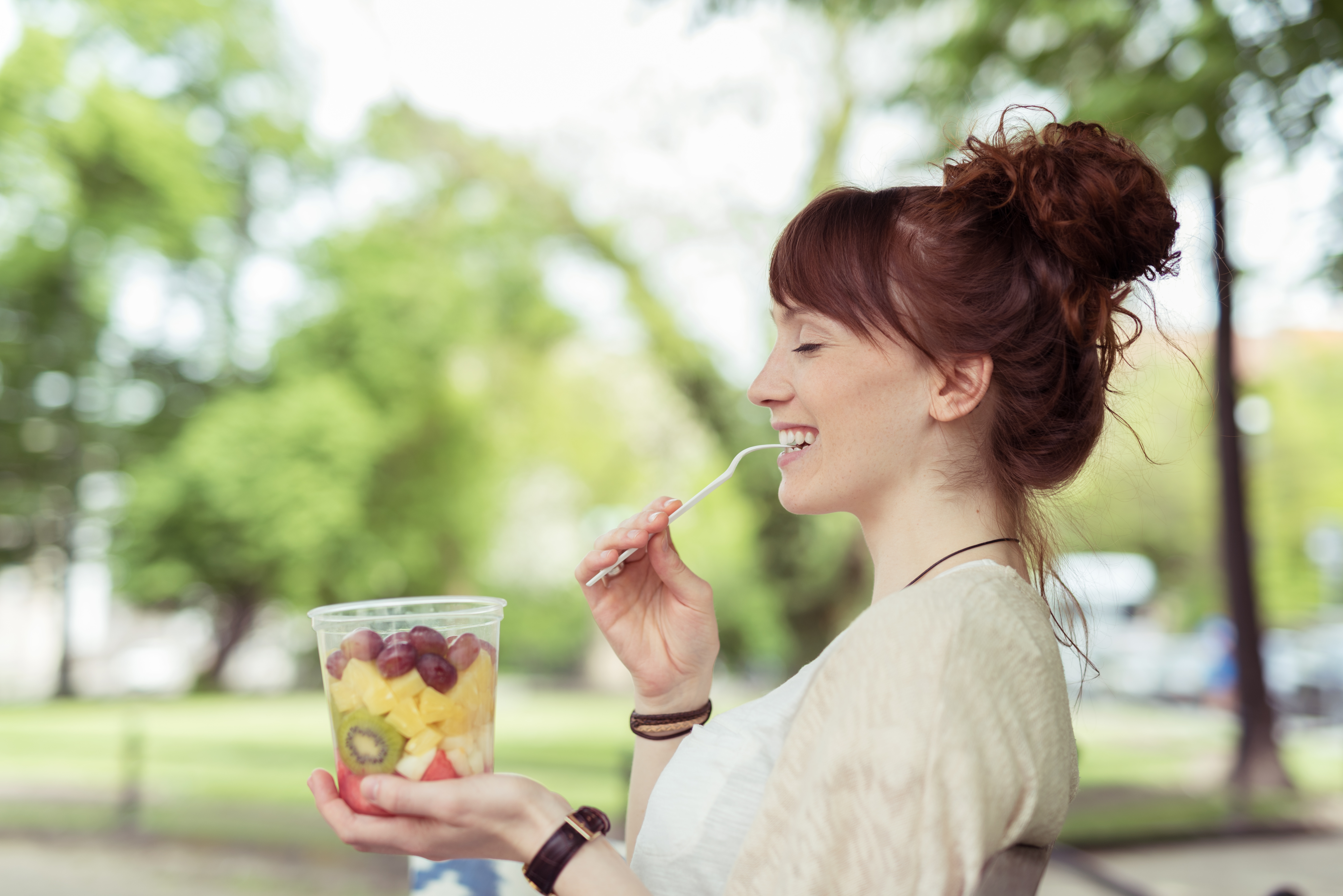 Woman eating fruit salad outdoors.