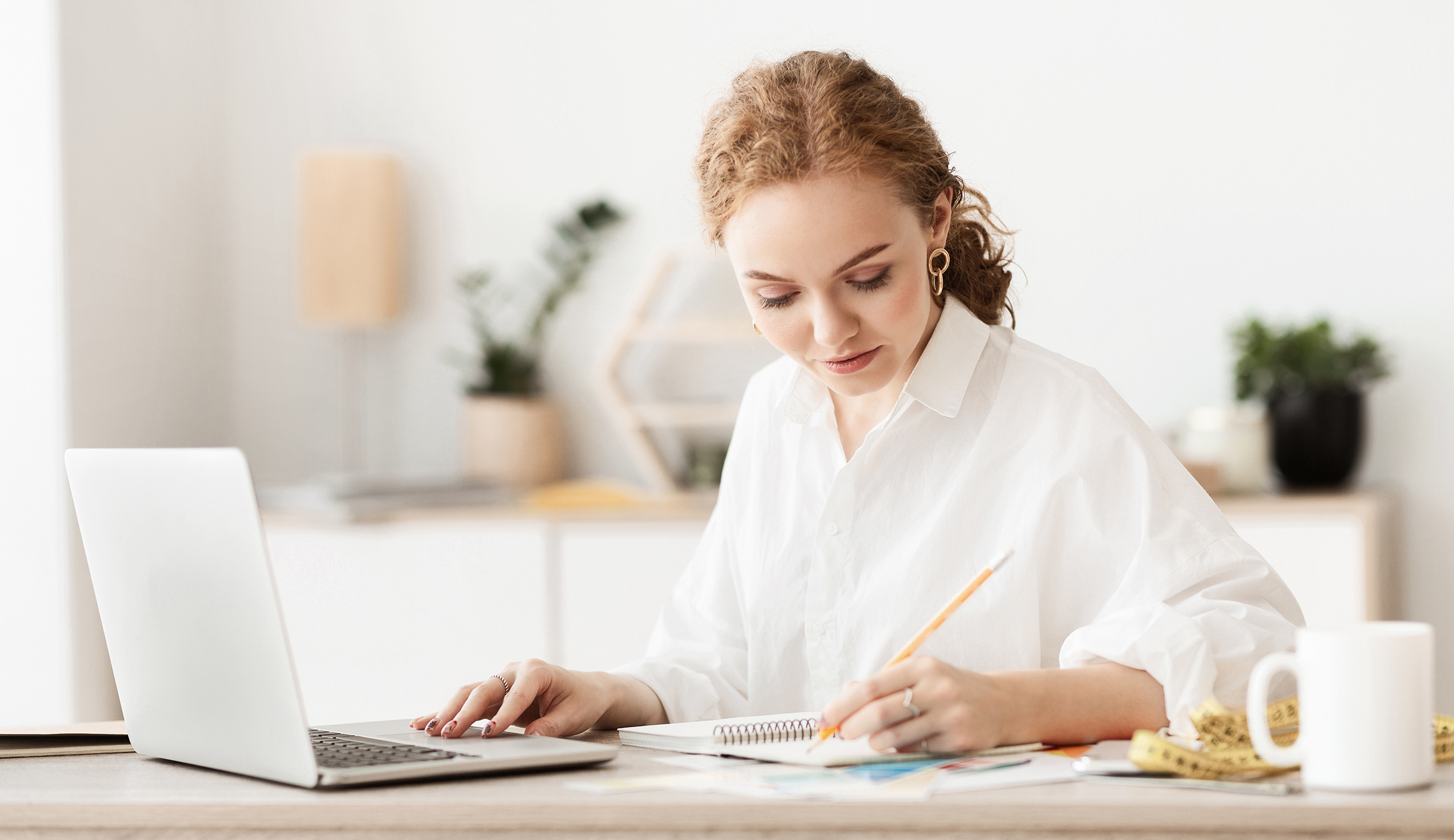 Woman writing whilst using laptop